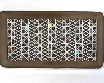 Könnte beinhalten: Rechteckige braune Keramik-Servierplatte mit weißem geometrischen Gittermuster. Das Gitter ist mit kleinen, farbigen quadratischen Fliesen in Rot, Gelb, Blau und Türkis akzentuiert. Die Platte hat einen weißen Rand.