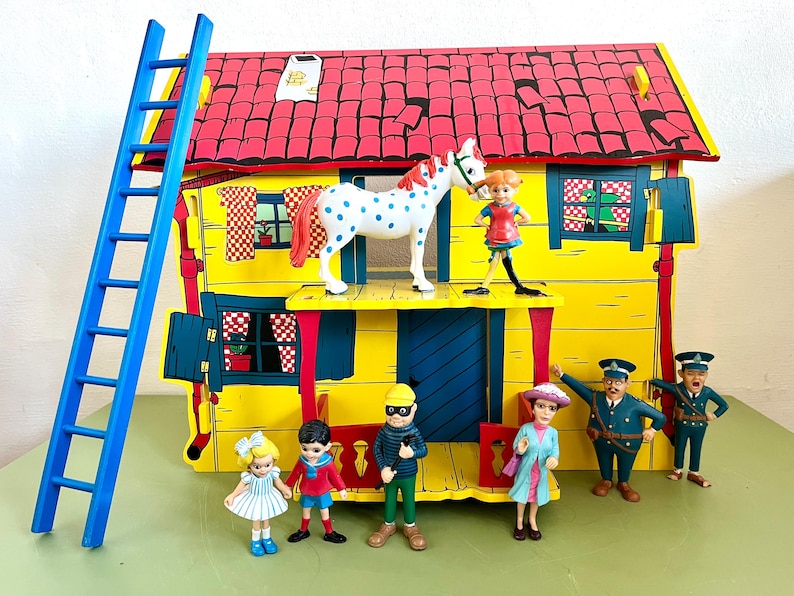 Op de afbeelding: Een kleurrijke speelset met een geel huis met een rood dak, een blauwe ladder en verschillende beeldjes. De beeldjes omvatten een paard met witte vlekken, een meisje, een jongen, een dief, een vrouw en twee politieagenten.
