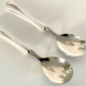 May include: A set of two silver salad serving utensils. The serving spoon has a rounded bowl and the serving fork has a wide, flat head with small teeth.