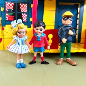 Op de afbeelding: Een kleurrijke speelgoedset met miniatuurfiguren en een geel gebouw. De figuren zijn onder meer een meisje in een gestreepte jurk, een jongen in een rode jas en een man in een gestreept shirt en masker met een gereedschap. De set heeft een speels en grillig ontwerp.