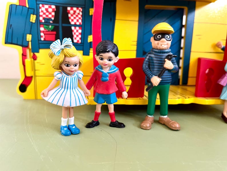 Op de afbeelding: Een kleurrijke speelgoedset met miniatuurfiguren en een geel gebouw. De figuren zijn onder meer een meisje in een gestreepte jurk, een jongen in een rode jas en een man in een gestreept shirt en masker met een gereedschap. De set heeft een speels en grillig ontwerp.