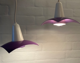 May include: Two purple and white pendant lights with a flower-shaped shade. The lights are hanging from the ceiling and are turned on.