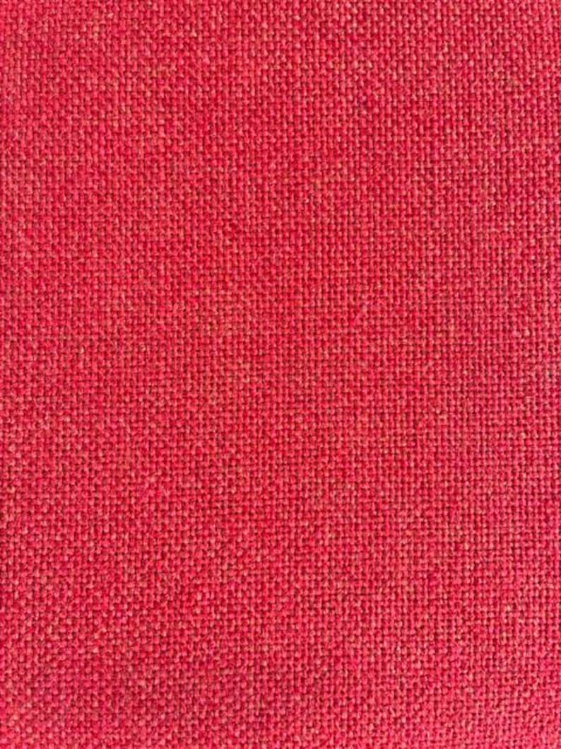 May include: A close-up shot of a red woven fabric. The texture is coarse and appears to be made of natural fibres. The weave is tight, creating a solid, uniform colour across the surface. The fabric has a slightly rough, tactile appearance.
