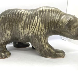 Op de afbeelding: Een keramieken berenbeeldje in tinten olijfgroen en bruin. De beer wordt afgebeeld in een loopstand, met gedetailleerde vachttextuur. Het beeldje is een decoratief item, geschikt voor weergave.