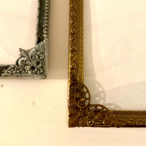 May include: Close-up of two ornate picture frame corners. One is silver with a textured finish, the other is gold with intricate scrollwork. Both frames have a vintage aesthetic and are set against a white background.