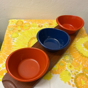 May include: A wooden serving tray with three ceramic bowls. The bowls are red and blue. The tray is brown and has a natural wood finish.