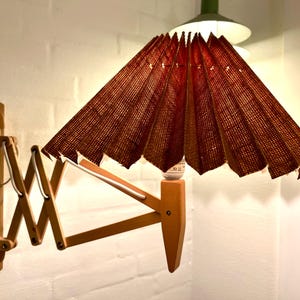 Peut inclure: Une lampe murale en bois avec un abat-jour en tissu brun. La lampe a un bras pliable et un cordon blanc.