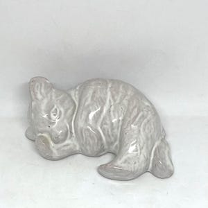 May include: A white ceramic mug with a black handle and the text "But First, Coffee" in a black, bold font. The mug is sitting on a wooden surface. The mug is approximately 4 inches tall.