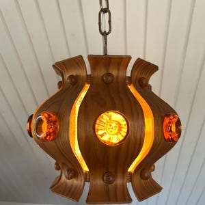 May include: A wooden pendant light with a geometric design and amber glass accents. The light is hanging from a chain.