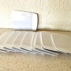 May include: A set of ten white rectangular plates stacked on top of each other. The plates are made of ceramic and have a smooth, glossy finish.