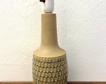 May include: A ceramic table lamp with a textured, brown and green glaze. The lamp has a white socket and a brown cord.