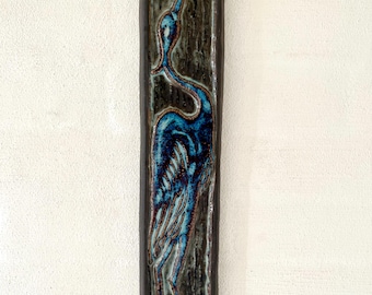 May include: A rectangular ceramic wall hanging featuring a stylized blue heron. The bird is depicted with intricate details against a dark, textured background. The piece has a dark brown border and a glossy finish.