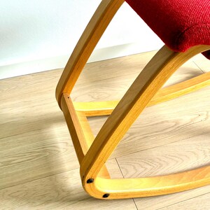 May include: A rocking chair with a red seat and a light-coloured wooden frame. The chair's frame is made of curved wood. The seat is a solid, deep red. The chair is on a light-coloured wooden floor.