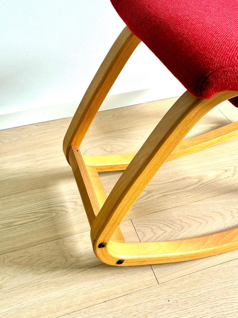 May include: A rocking chair with a red seat and a light-coloured wooden frame. The chair's frame is made of curved wood. The seat is a solid, deep red. The chair is on a light-coloured wooden floor.