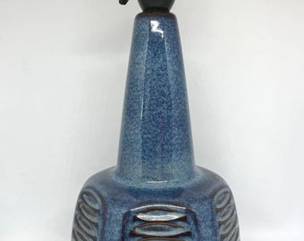 May include: A blue ceramic table lamp with a black lamp holder. The lamp has a textured, patterned design on the base and a conical shape leading to the lamp holder. The lamp is approximately 12 inches tall.
