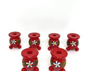 May include: Six red wooden candle holders with white flowers and green leaves painted on them. Each holder has three legs.