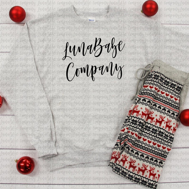 May include: A gray sweatshirt with the text "LunaBabe Company" printed on the front. A pair of white, red, and black patterned pajama pants with reindeer designs are lying next to the sweatshirt.