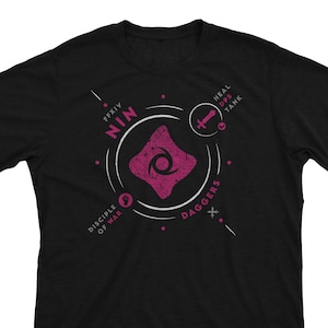 May include: Black t-shirt with a white graphic design featuring a pink symbol and the text "NIN" and "DAGGER" with the words "DISCIPLE OF WAR" and "HEAL DPS TANK" in smaller text.
