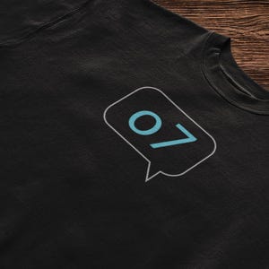 May include: Black sweatshirt with a white outline of a speech bubble containing the number "07" in blue.