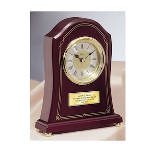 May include: A mahogany wood clock with a gold trim and a gold face. The clock has a plaque with the text "Jamie C Taylor Ten Years of Dedicated Service Malibu Country Club May 2012".