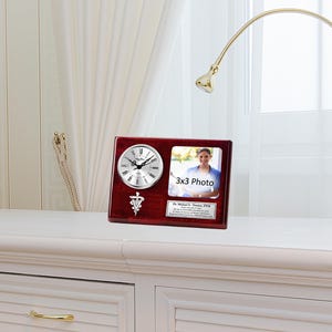 May include: A mahogany desk clock with a silver face and a silver medical symbol. The clock has a 3x3 inch photo frame with a woman in it. The text "3x3 Photo" is printed on the frame. The text "Dr. Michael E. Thomas, DVM" is printed on the plaque below the photo frame.