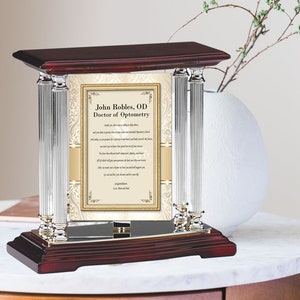 May include: A mahogany wood plaque with silver columns and a gold-framed certificate. The certificate reads "John Robles, OD Doctor of Optometry" and includes a poem about the importance of vision.