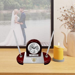 May include: A mahogany desk clock set with a silver clock face, two silver pens, and a silver nameplate that reads "Timothy J. Smith, OD, Doctor of Optometry".