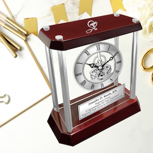 May include: A mahogany desk clock with a silver face and a silver frame. The clock has a skeleton movement and a silver plaque with the text "Jennifer D. Smith, RN Registered Nurse Congratulations On Your Graduation Engraved Desk Clocks by AliGetFrames.com".