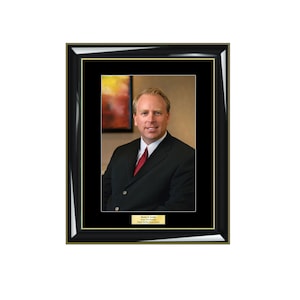 May include: A framed portrait of a man in a black suit and red tie. The man is smiling and looking at the camera. The frame is black with a gold trim. The text on the plaque below the portrait reads "Doctor C. Laviolette, President, Digital Network Board Systems."