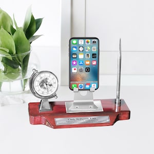 May include: A mahogany desk organizer with a silver phone stand, a silver clock with a world map design, and a silver pen holder. The organizer has a personalized plaque that reads "Cindy McDaniels, ESQ. Engraved Desk Clocks by A&A Designs. Distributor of Personalized and Recognition Award Clocks."