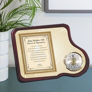 May include: A mahogany-colored plaque with a gold-framed certificate and a clock. The certificate reads "John Robles, OD Doctor of Optometry" and includes a poem. The clock has a gold rim and white face with black numbers.
