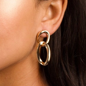 May include: Gold chain link earrings with two oval-shaped links. The earrings are dangling and have a polished finish.