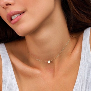 Peut inclure: Un collier ras de cou en chaîne dorée avec un petit pendentif rond orné d'une seule lettre.