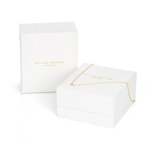 Puede incluir: Caja de joyer&iacute;a blanca con el texto "darling jewelry studio" en la tapa. La caja est&aacute; abierta y hay un collar de cadena dorada dentro.