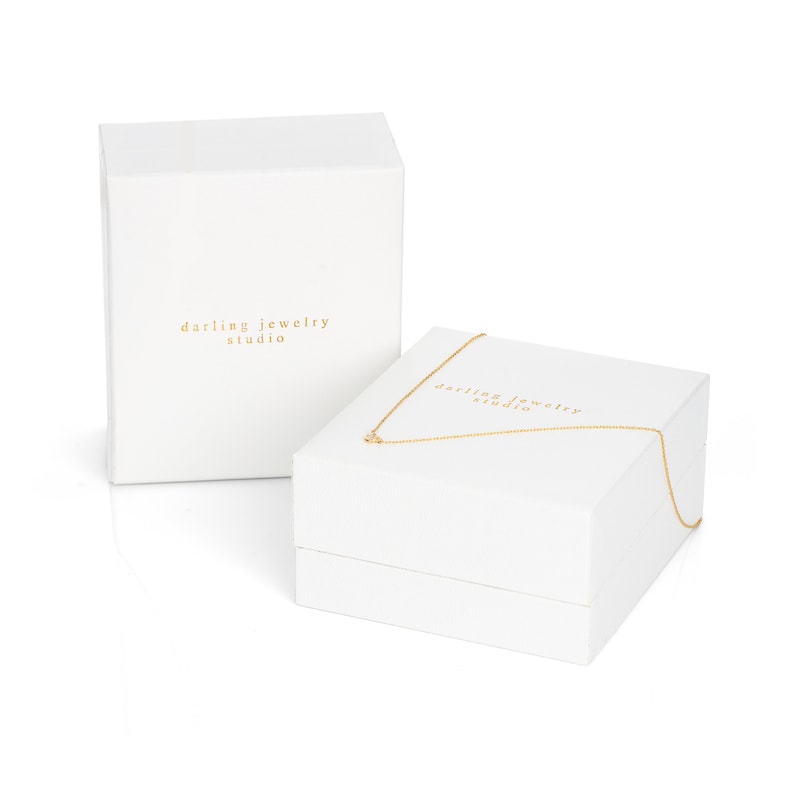 Puede incluir: Caja de joyer&iacute;a blanca con el texto "darling jewelry studio" en la tapa. La caja est&aacute; abierta y hay un collar de cadena dorada dentro.