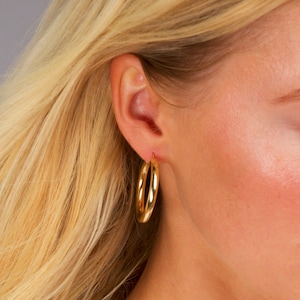May include: Gold hoop earrings worn in a person's ear. The earrings are a simple, classic design.