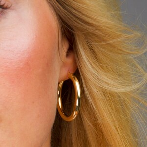 May include: A pair of gold hoop earrings. The earrings are thick and have a smooth, polished finish.