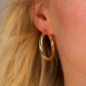 May include: Gold hoop earrings worn in a person's earlobe.