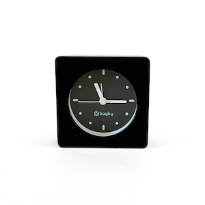 May include: A black square clock with white hands and a white face. The clock face has black numbers and the word "bagby" in white letters.