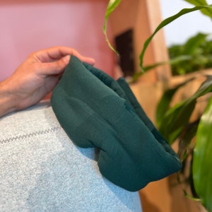 May include: A dark green sleep mask made of soft fabric. The mask is curved to fit comfortably over the eyes.