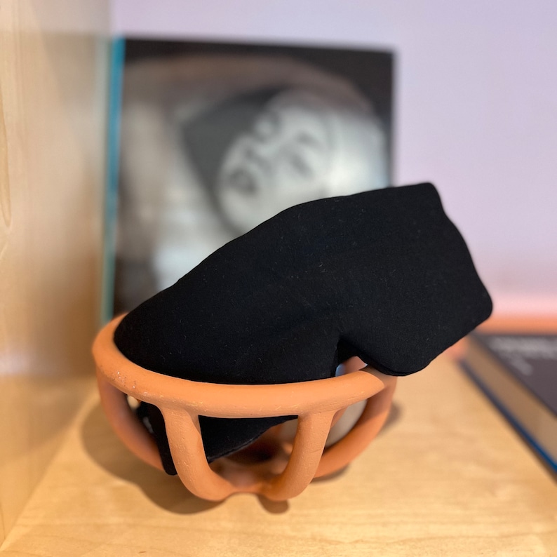 May include: A black sleep mask in a terracotta-colored ceramic bowl. The bowl has a unique, organic shape with a wide opening and a narrow base.