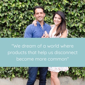 May include: A couple stands in front of a green leafy wall. The woman is wearing a white floral dress and the man is wearing a blue button-down shirt and jeans. The text "We dream of a world where products that help us disconnect become more common" is displayed in front of them.