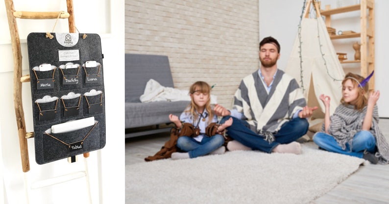 Op de afbeelding: Een donkergrijze vilten organizer met meerdere vakken met de labels "Marie", "Daddy", "Liona" en "Tablet". De organizer hangt aan een houten ladder. Op de achtergrond mediteert een gezin op een wit tapijt.