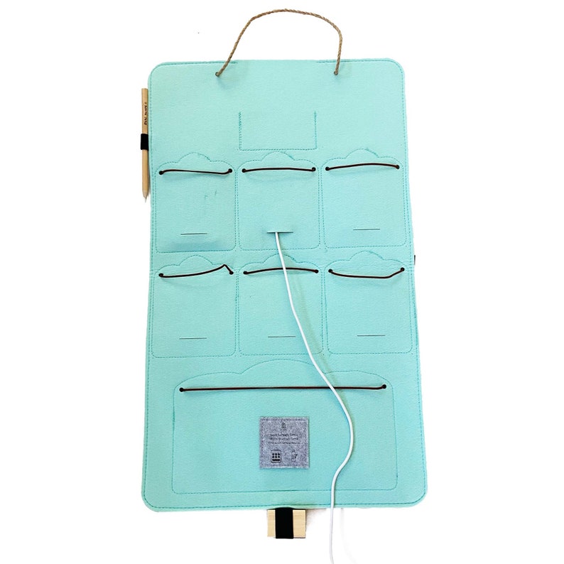 Op de afbeelding: Een lichtblauwe vilten organizer met meerdere vakken en een jute handvat. Het heeft een houten potlood en een wit snoer. De organizer is ontworpen om op te hangen en heeft een klein label aan de onderkant.