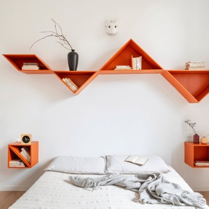 Peut inclure: Un lit blanc avec une couverture blanche et une couverture grise. Le lit est contre un mur blanc avec des &eacute;tag&egrave;res triangulaires orange contenant des livres. Il y a une petite horloge sur la table de chevet.