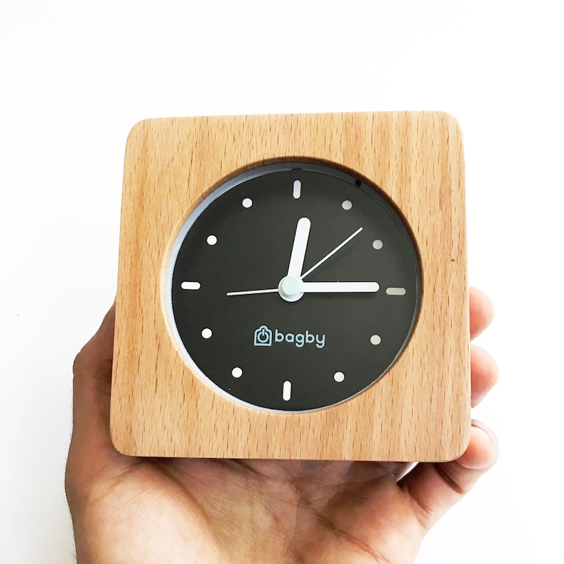 Peut inclure: Un r&eacute;veil en bois avec un cadran noir et des aiguilles blanches. L'horloge a un logo blanc qui dit "bagby" sur le cadran.