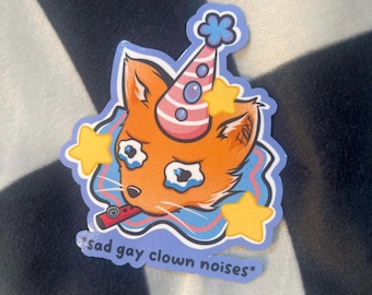 May include: A die-cut sticker featuring an orange fox head wearing a pink and white striped party hat with a blue pom-pom. The fox has blue teary eyes, holds a red whistle, and is surrounded by yellow stars. The text reads *sad gay clown noises*.