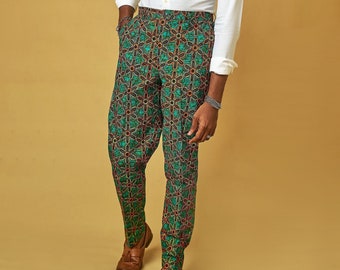 Puede incluir: Un hombre con una camisa blanca abotonada y pantalones verdes con un patrón geométrico. Está de pie frente a un fondo marrón claro.
