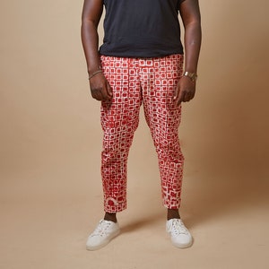 May include: A person wearing a black t-shirt with a gold chain necklace, red and white patterned pants, and white sneakers.