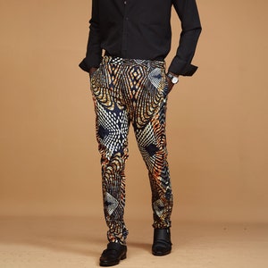May include: A man wearing a black long-sleeved button-down shirt and patterned pants. The pants are black with gold and orange geometric designs.